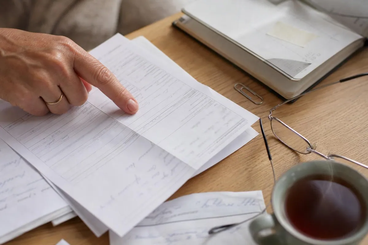 Gros plan sur des documents administratifs français empilés, formulaire annoté au crayon, ordonnance pliée et agenda ouvert marqué par un morceau de ruban adhésif